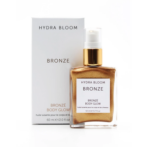 Bottle of Bronze Body Glow | Hydra Bloom with golden shimmering body oil and matching white and gold pump packaging displayed against a white background.