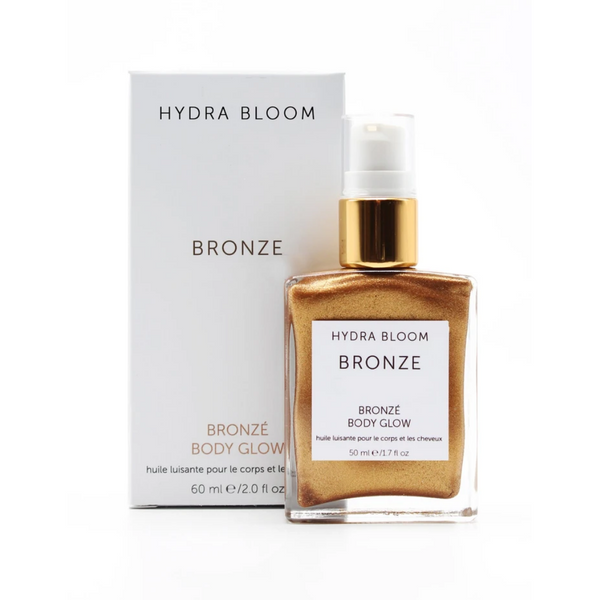 Bottle of Bronze Body Glow | Hydra Bloom with golden shimmering body oil and matching white and gold pump packaging displayed against a white background.