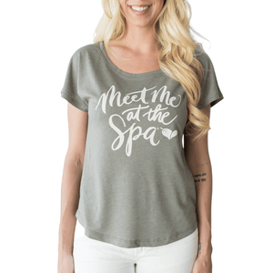 Woman wearing a soft gray Meet Me at the Spa Calligraphy Women's T-Shirt | Lucky Owl with white script text, paired with white pants, smiling with long blonde hair.