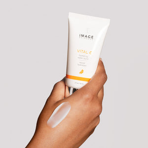 Hand holding a tube of VITAL C hydrating water burst | IMAGE Skincare with a swatch of hydrating cream on the back of the hand, showcasing skincare product texture.