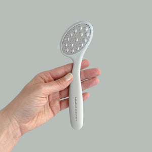 Hand holding the Smooth Things Over | Barefoot Scientist foot care tool with ergonomic handle and textured surface for skincare and body care wellness.