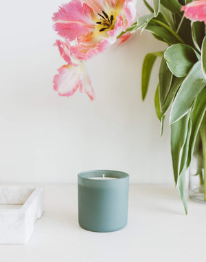 Evergreen + Eucalyptus Dignity Series Glass Jar Soy Candle | Calyan Wax Co. - 5.3 oz placed on a white surface next to a marble tray with pink and white flowers in the background.