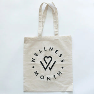 Natural cotton tote bag with black Wellness Month logo and heart design, promoting wellness and self-care, named Wellness Month Tote Bag | Wellness Month.