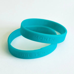 Two blue silicone bracelets stacked on a white surface, featuring embossed messages promoting wellness and labeled Silicone Bracelets | Wellness Month