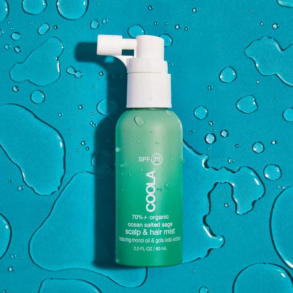Bottle of Scalp & Hair Mist Organic Sunscreen SPF 30 | COOLA with a spray nozzle on a wet blue surface, highlighting organic skincare and sun protection for hair and scalp.