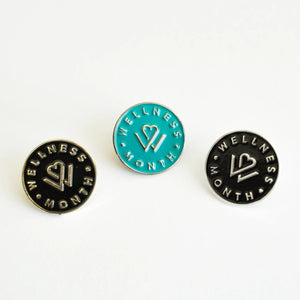 Set of three round enamel pins in black and teal colors featuring a heart and wellness design with the text "WELLNESS MONTH," perfect for promoting self-care and wellness themes, Enamel Pins | Wellness Month.