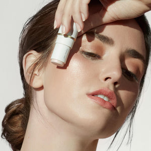 Woman with glowing skin holding Glow Time Blush Stick | Jane Iredale near her cheek, showcasing natural makeup and radiant skincare effect.