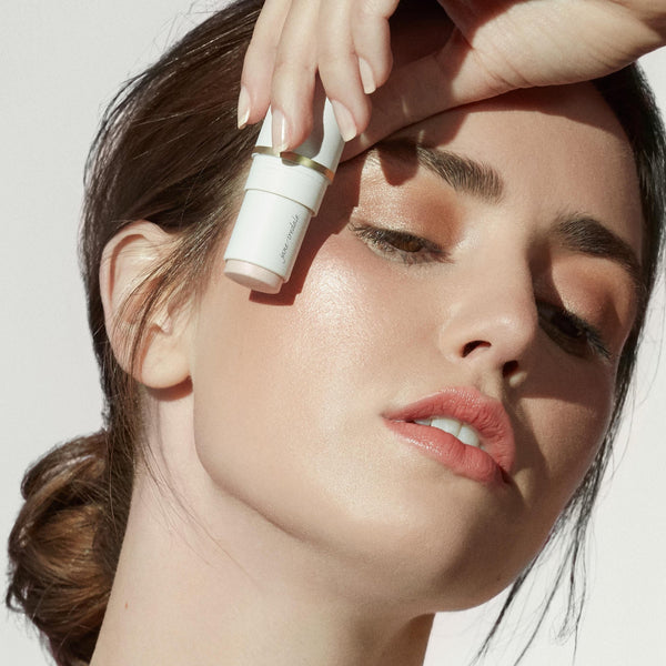 Woman with glowing skin holding Glow Time Blush Stick | Jane Iredale near her cheek, showcasing natural makeup and radiant skincare effect.