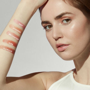 Close-up of a woman's arm showing swatches of five blush shades labeled Mist, Ethereal, Enchanted, Aura, and Glorious, showcasing Glow Time Blush Stick | Jane Iredale’s natural, radiant finish.