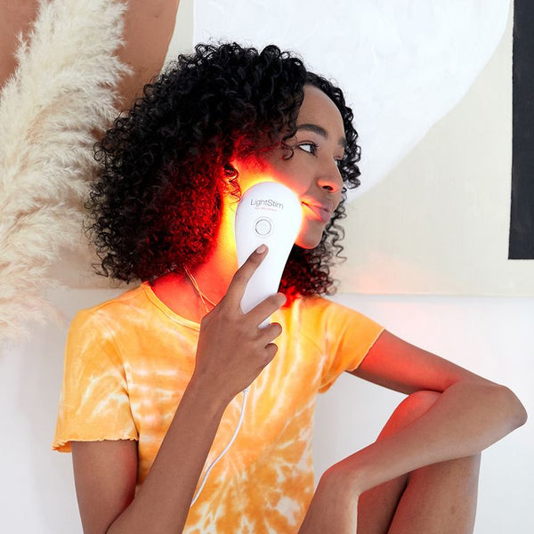 Woman using the LightStim For Wrinkles | LightStim device on her cheek, showcasing skincare and wellness with red light therapy for facial rejuvenation.