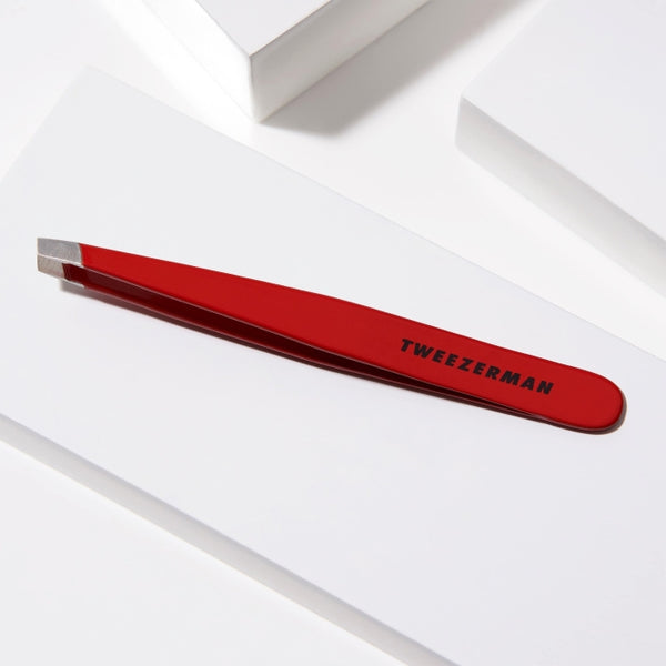 Red Slant Tweezer | Tweezerman with precision tips resting on a white geometric surface, designed for accurate eyebrow grooming and skincare routines.